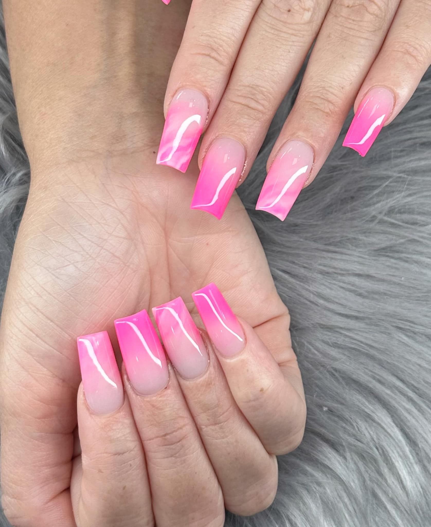 Close-up of hands showing long, square-shaped acrylic nails with a bright pink ombre design fading into a clear base.