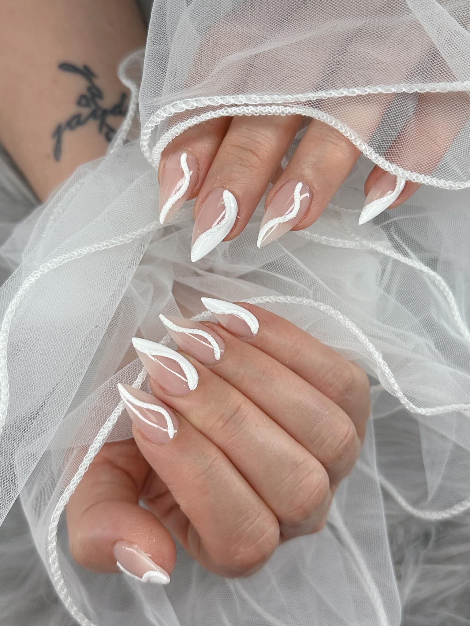 Close-up of almond-shaped nails featuring white abstract, wavy line art over a translucent, neutral base.