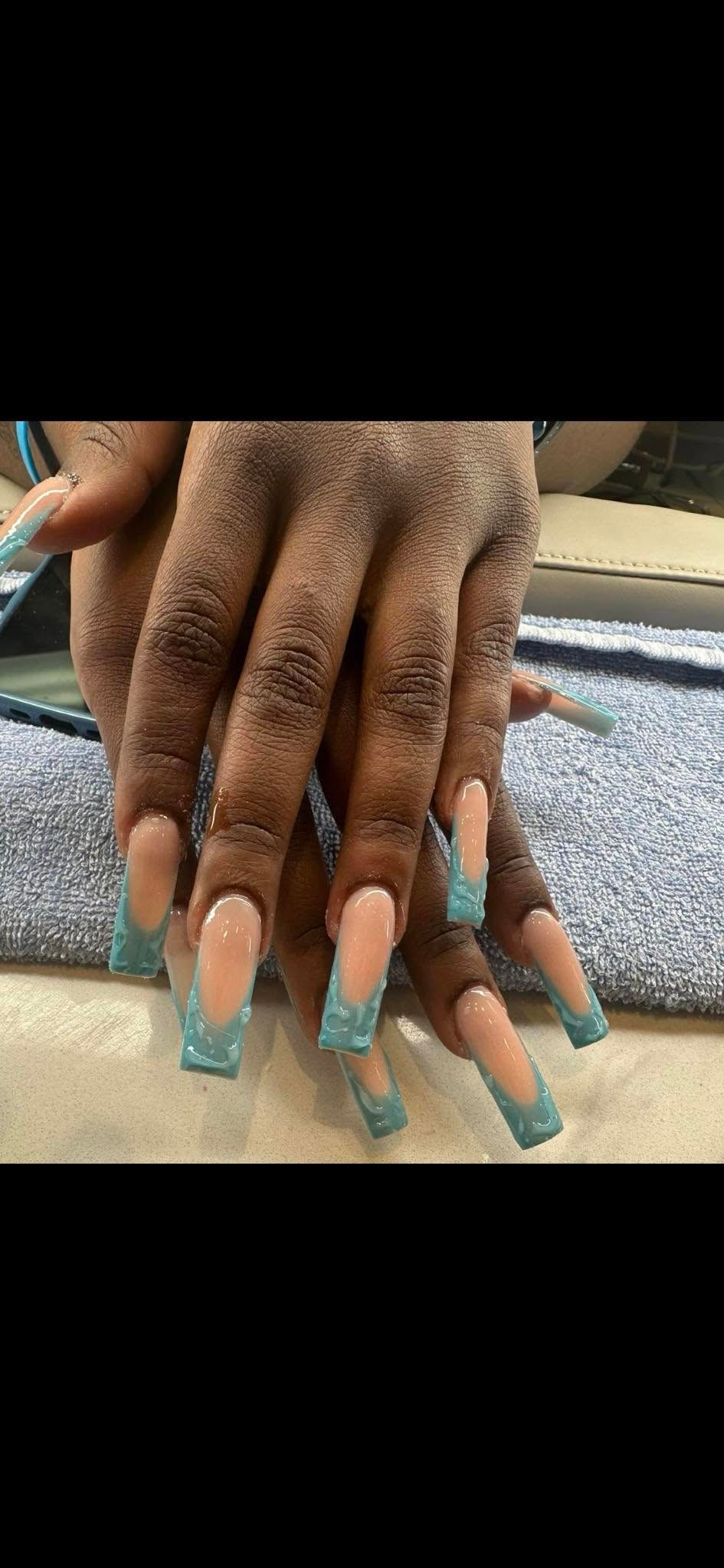 Close-up of long, square-shaped acrylic nails with a turquoise French tip design featuring small sparkling accents.