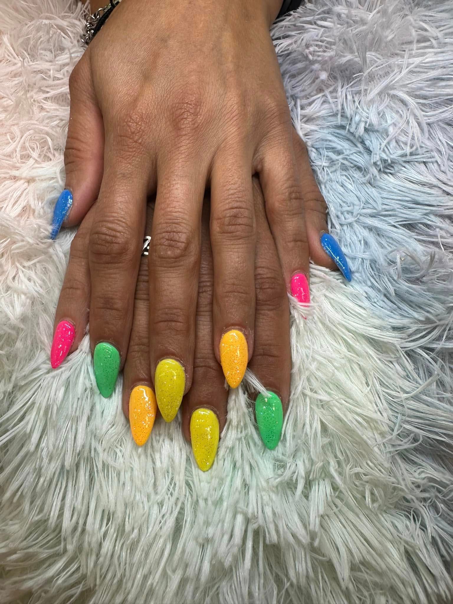 A hand displays long, almond-shaped nails painted in a variety of vibrant neon colors against a white shaggy background.