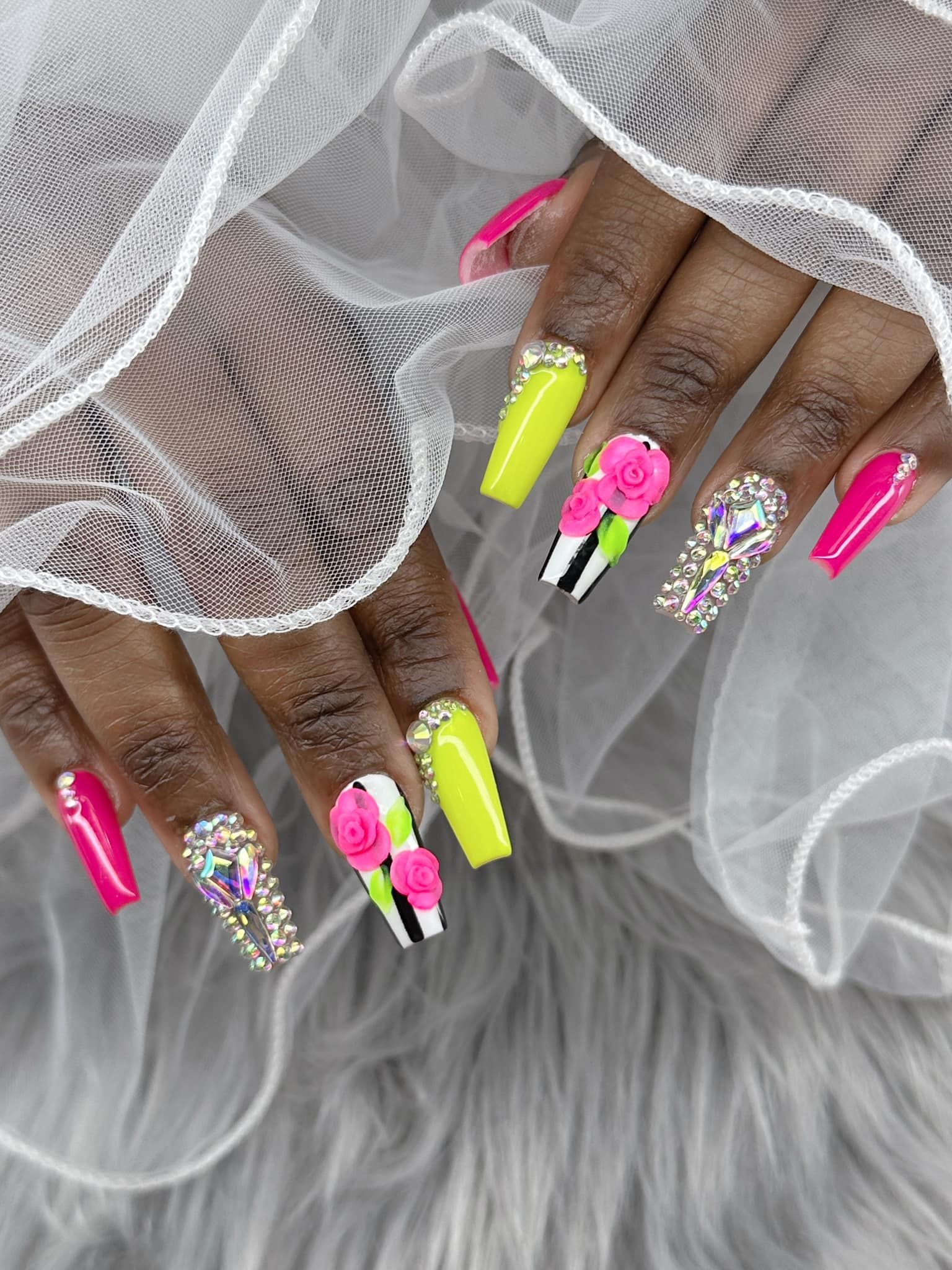 Long, square-shaped acrylic nails painted in bright neon green and pink, featuring crystal accents and 3D floral designs.