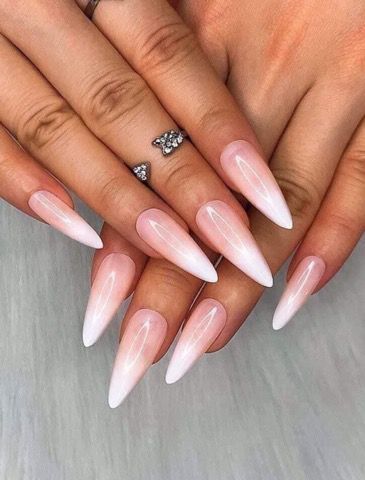 Close-up of long, pointed stiletto nails with a smooth, soft pink to white ombre design.