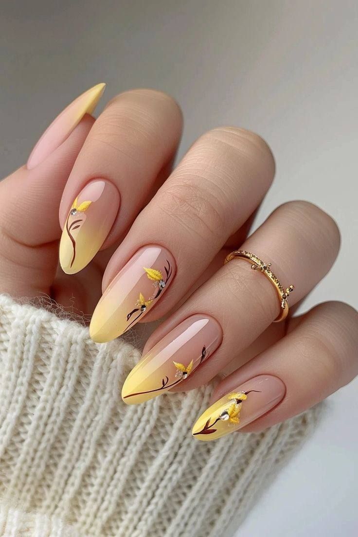 Hand with almond-shaped nails featuring a yellow-to-nude gradient, delicate black stems, and yellow flower accents.