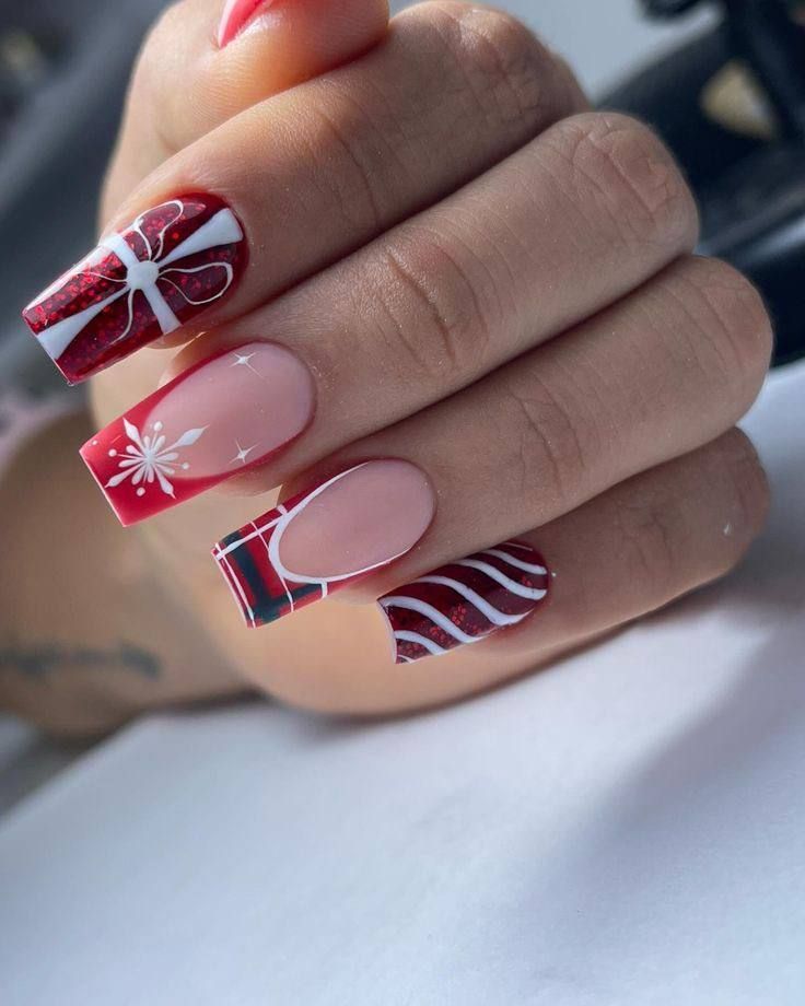 A hand with long, square-shaped nails featuring festive Christmas-themed art in red, white, and black patterns.