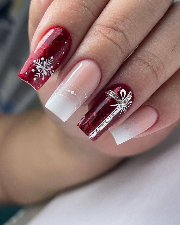 Close-up of fingernails with a festive Christmas design featuring deep red glitter, white ombré, a snowflake, and a ribbon.