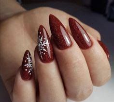 Almond-shaped nails painted in glittery deep red, featuring delicate white snowflake designs on the thumb and ring finger.
