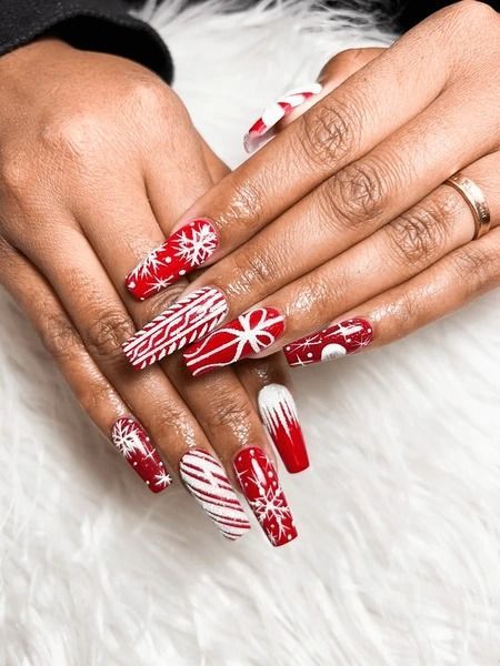 Hands display long, rectangular-shaped nails with festive red and white holiday designs including snowflakes and stripes.