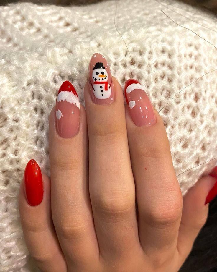 A hand with almond-shaped nails features Santa hat French tips on the sides and a snowman design on the middle finger.