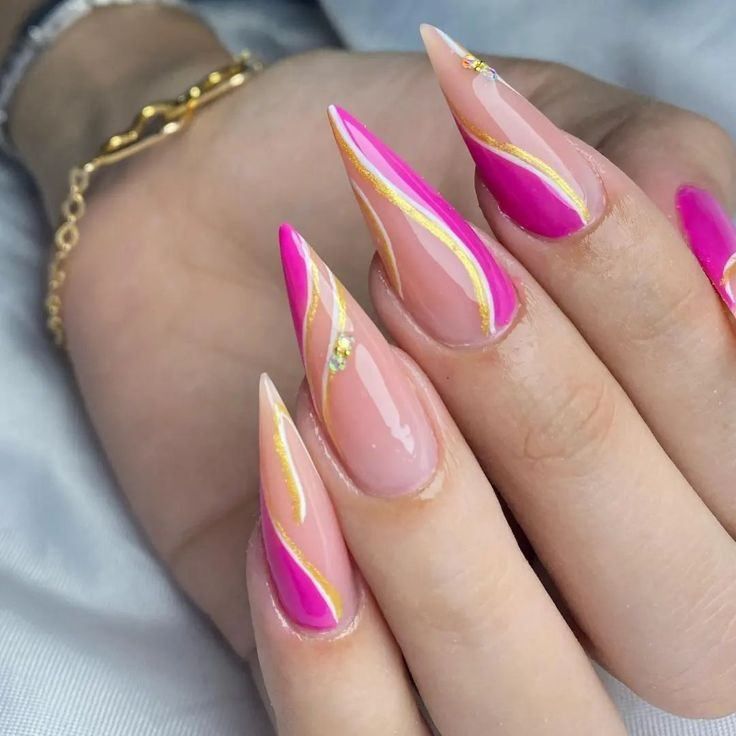 Stiletto-shaped nails with a nude base, vibrant pink wavy accents, gold line detailing, and small rhinestone embellishments.