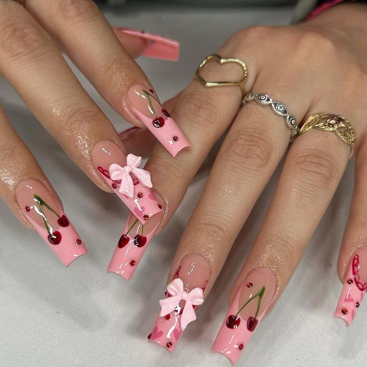 Long, square-tipped nails featuring pink French tips, hand-painted red cherries, and small, 3D light pink bows.