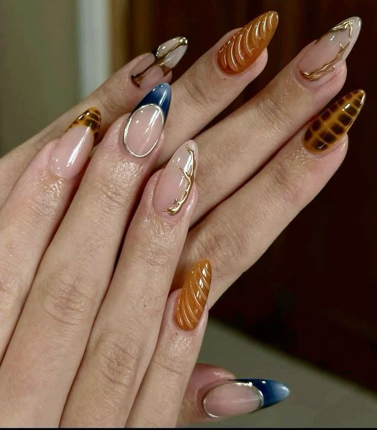 Close-up of hands showing almond-shaped nails with intricate designs, including textured amber, blue tips, and gold accents.