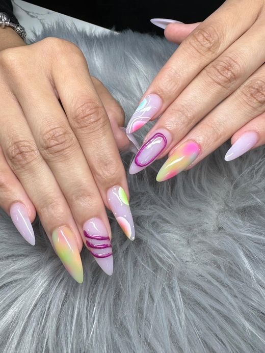 Stiletto nails with a pastel gradient, pink swirling accents, and a clear base, resting on a gray faux fur background.