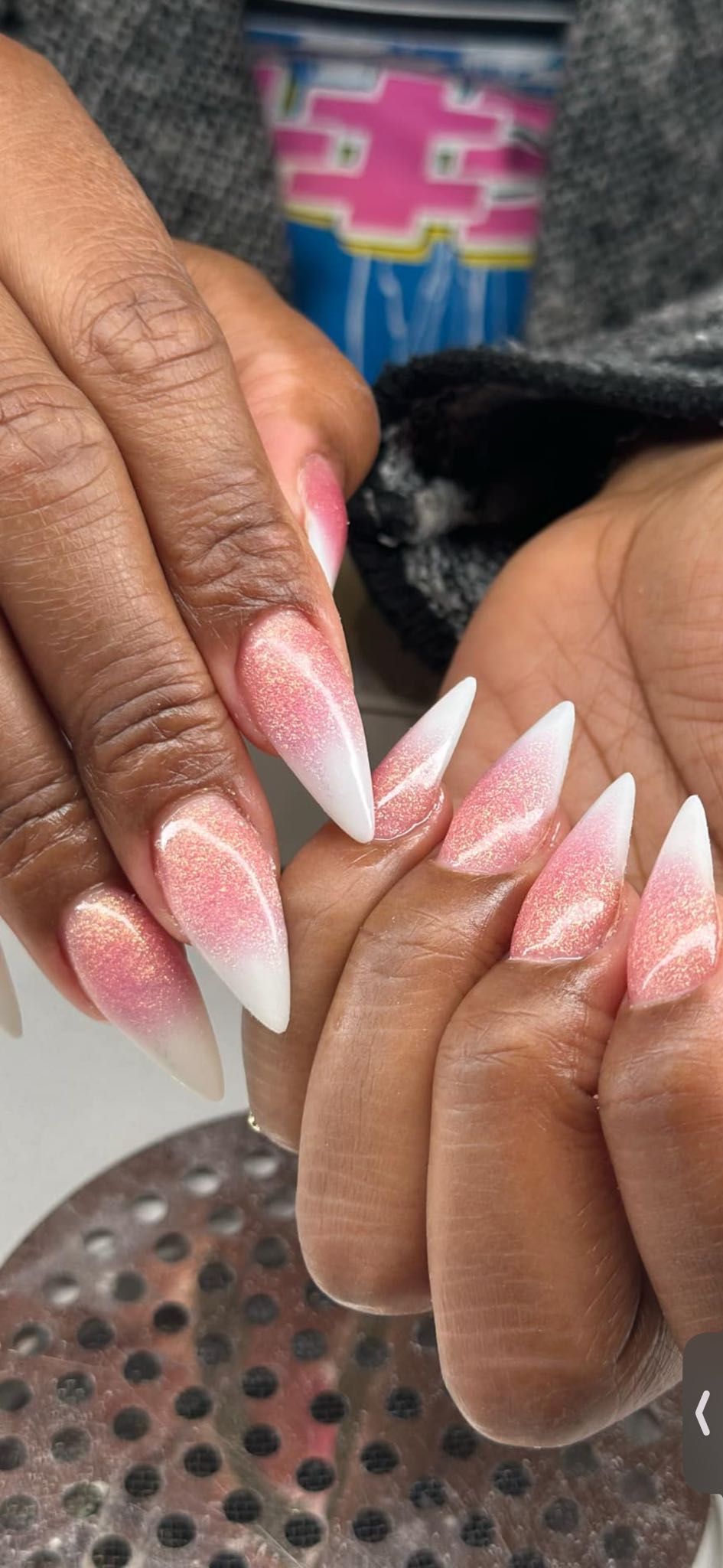 Stiletto-shaped nails with a pink and white glitter ombre design, shown on both hands.