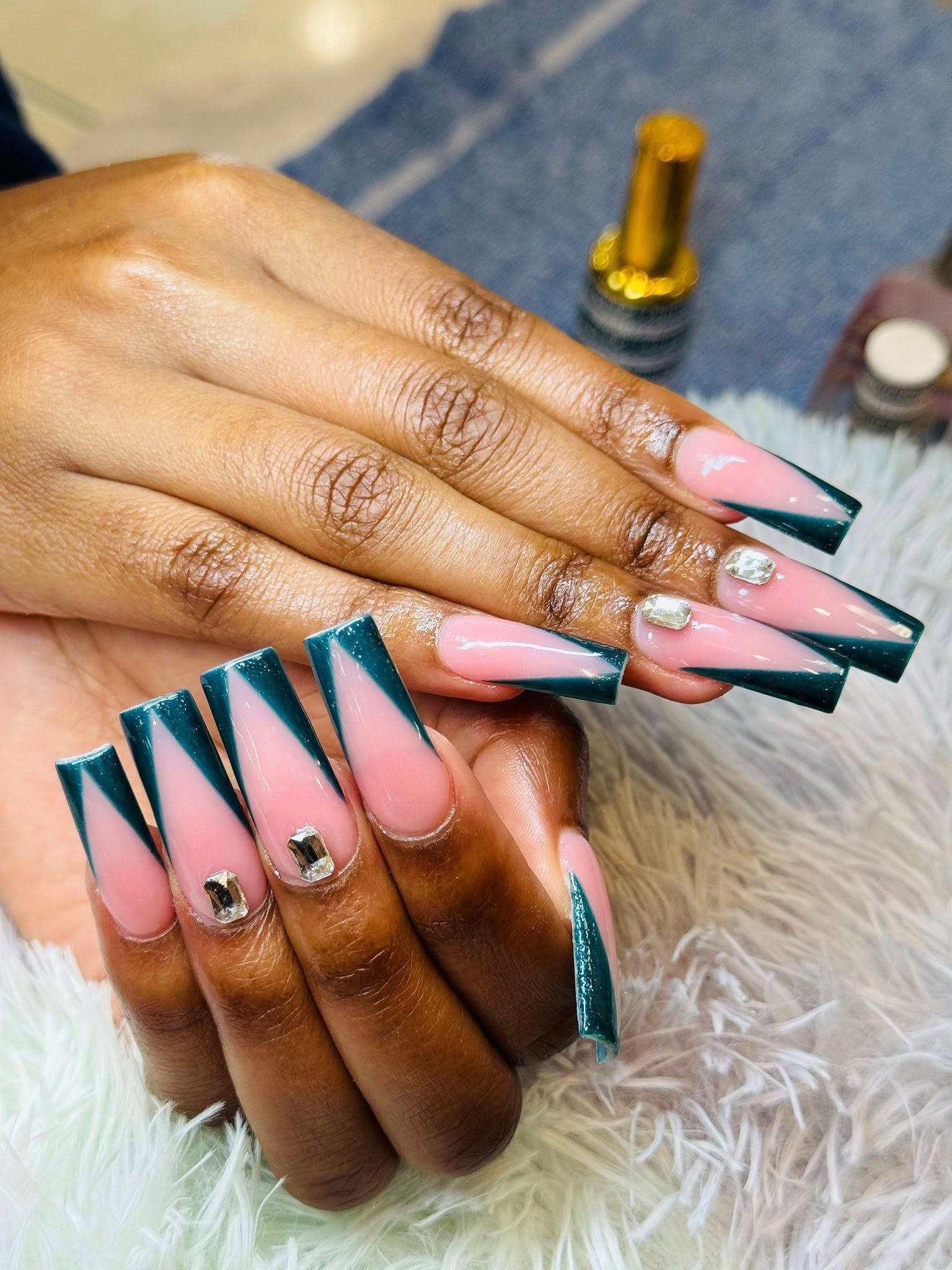 Close-up of long, square-tipped nails with a pink and dark green V-shaped French manicure, accented by small silver gems.