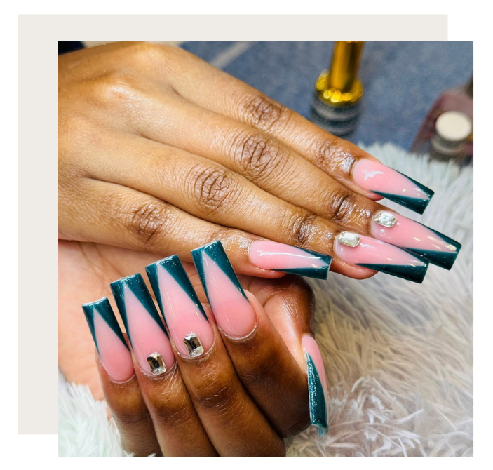 Hands showing long, coffin-shaped nails with a dark green V-shaped French tip design and rhinestone accents.