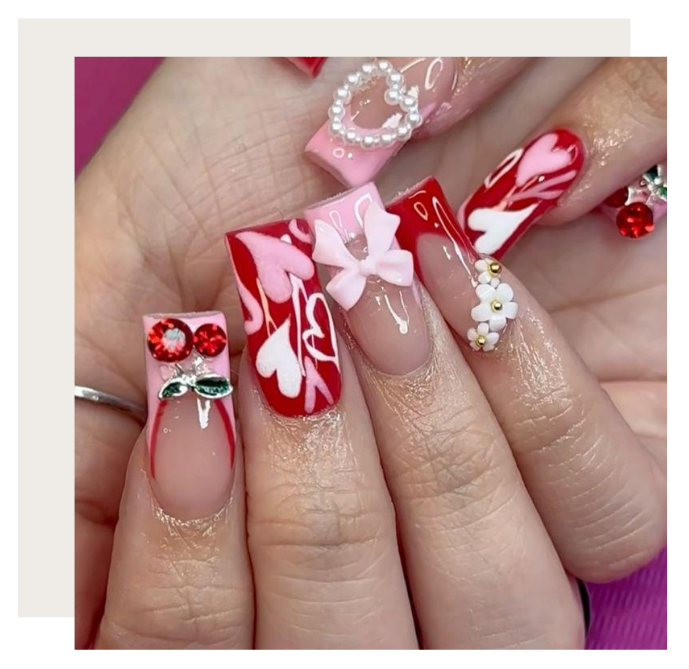 Square-shaped nails featuring red and pink heart patterns, 3D bows, cherry charms, pearls, and white floral embellishments.