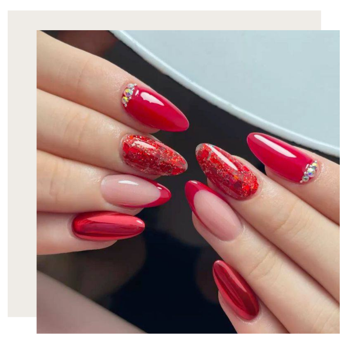 Two hands displaying almond-shaped nails in a variety of red finishes, including chrome, glitter, and French tips.