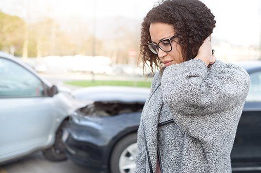 A woman is standing in front of a car that has been involved in a car accident.
