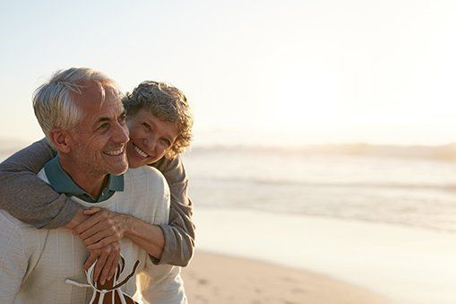 A man is giving a woman a piggyback ride on the beach.