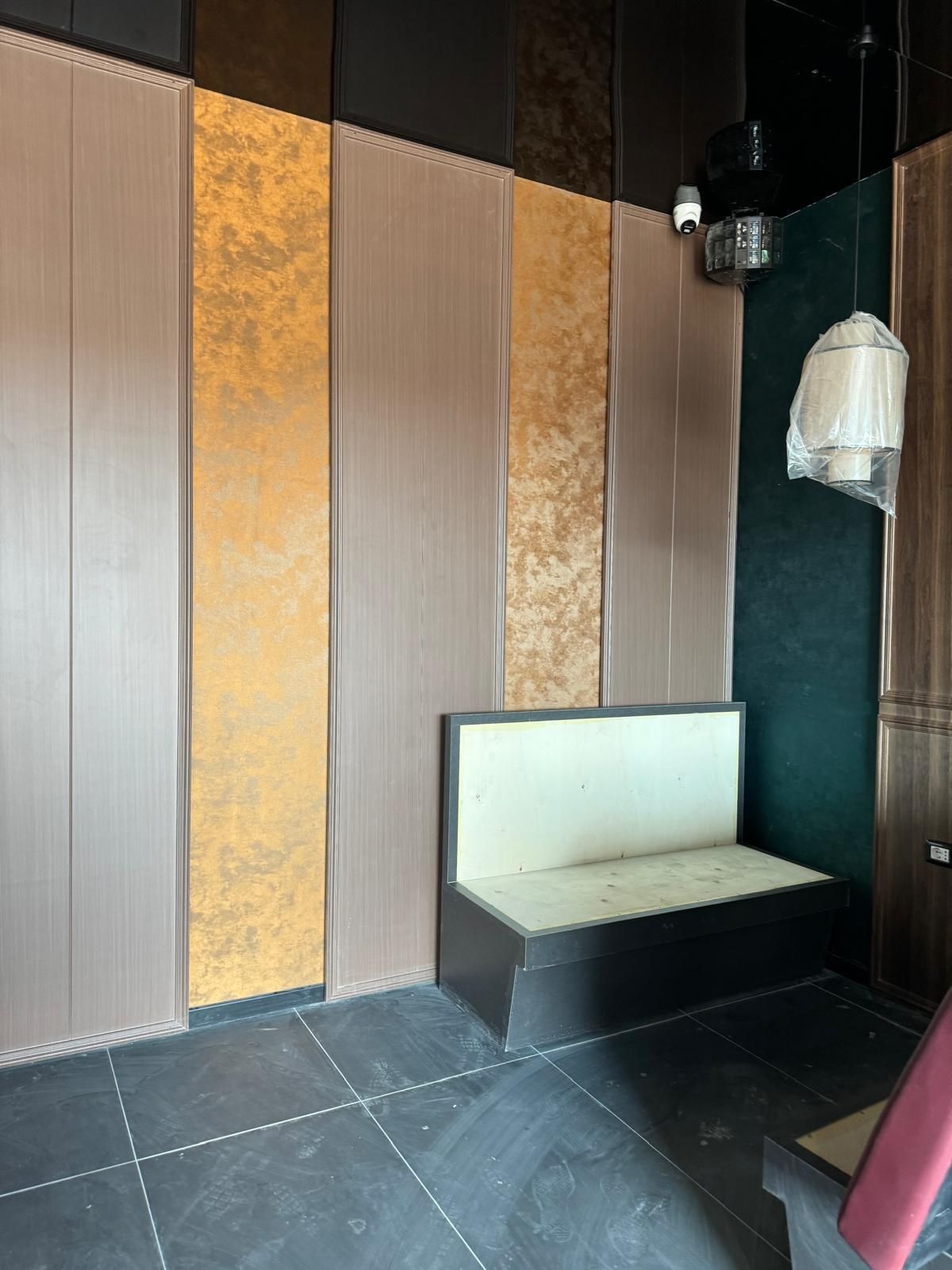 Interno con pannelli murali dorati e grigi, una panca nera integrata con cuscino bianco e una lampada a sospensione.