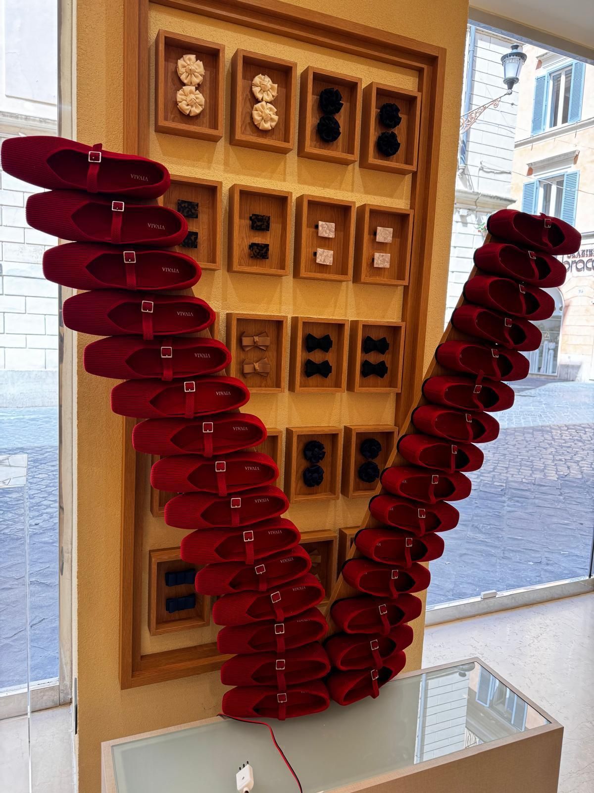 Scarpe rosse disposte a V su un espositore, con altre scarpe e accessori su una parete.