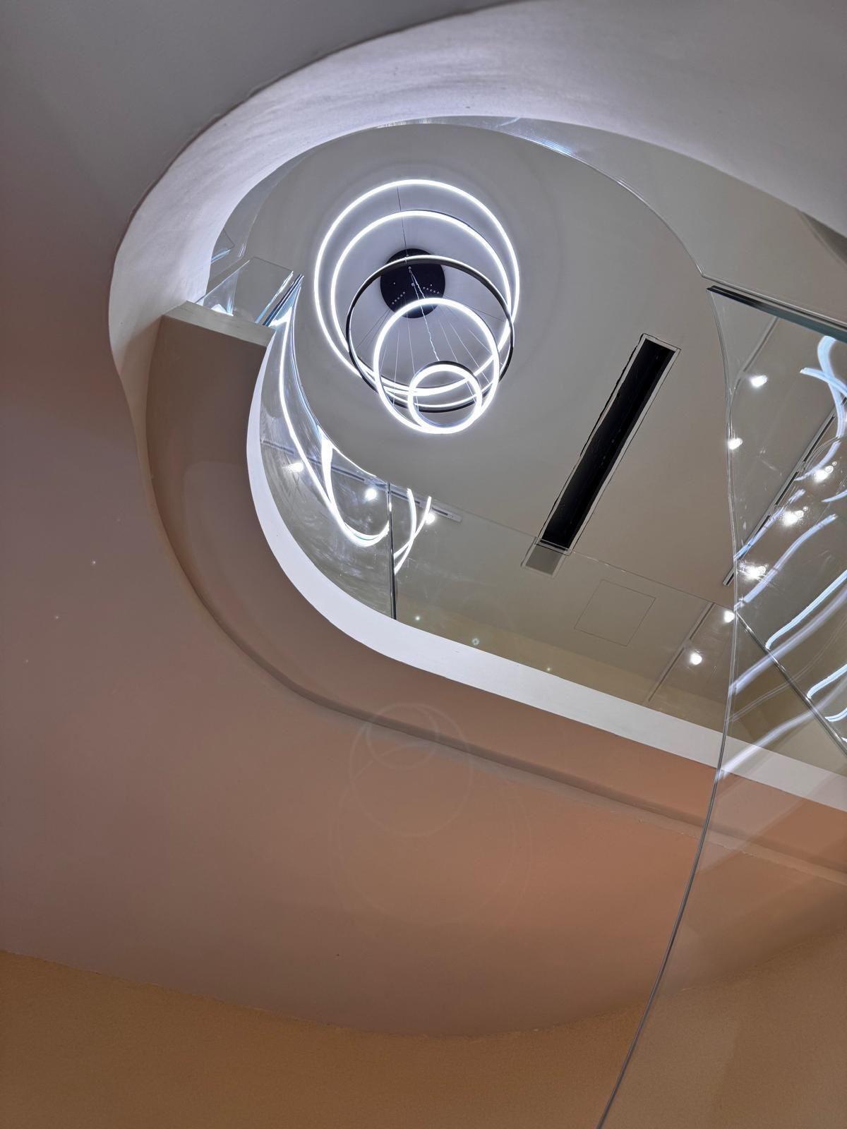 Scala a chiocciola con luci circolari moderne; ringhiere bianche e in vetro.