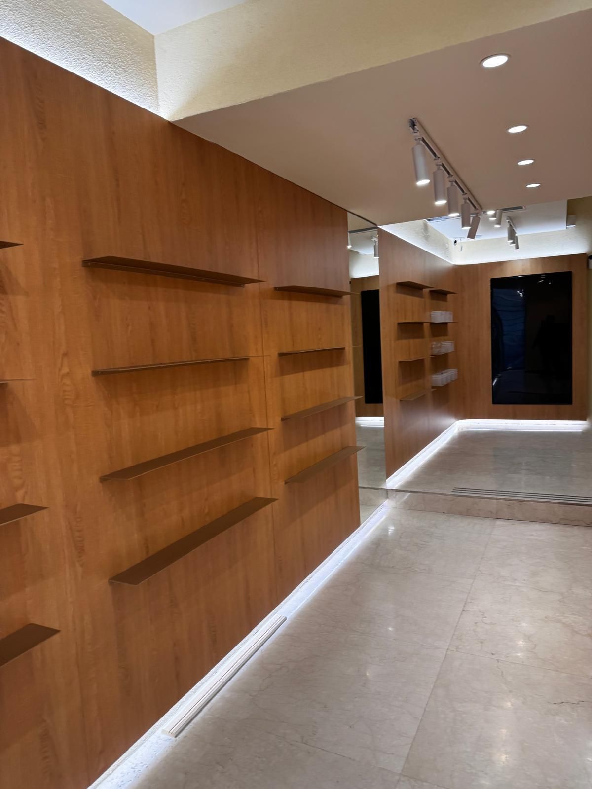 Interno vuoto di un negozio con pareti rivestite in legno, scaffali e illuminazione da incasso.