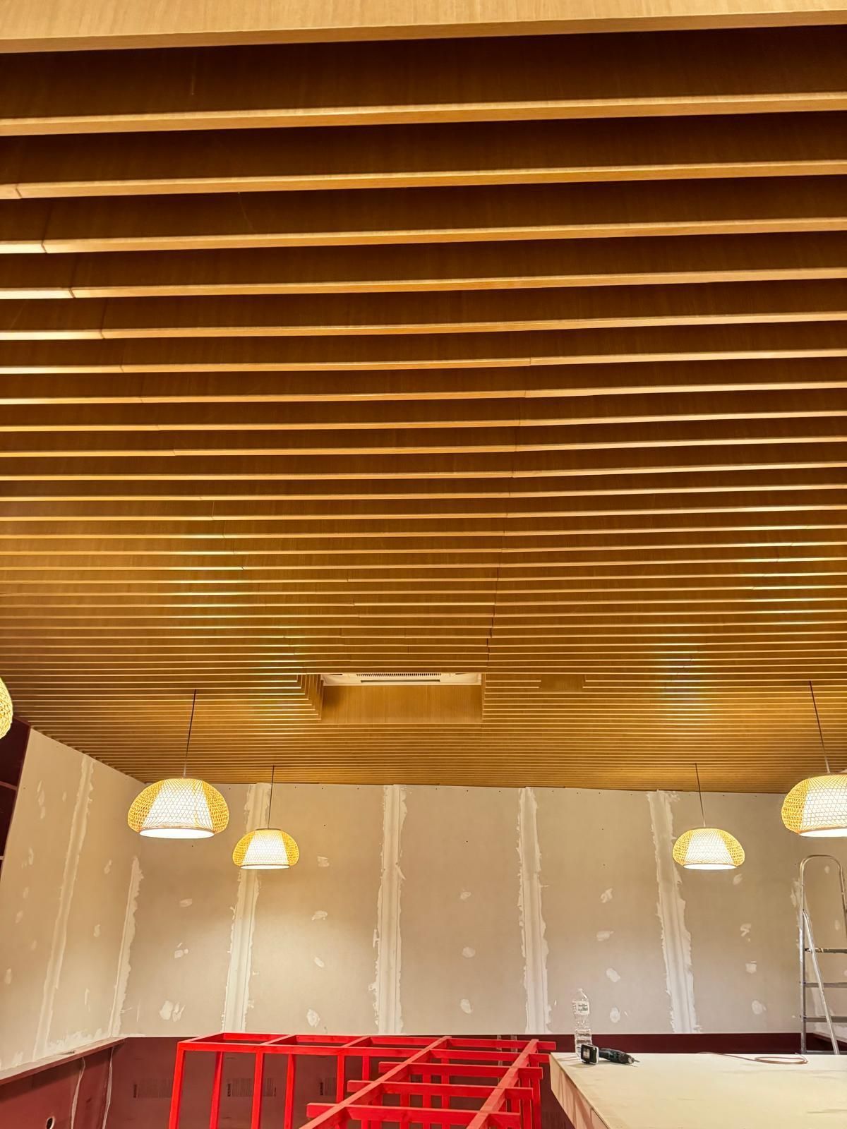 Soffitto con doghe in legno e luci pendenti; struttura rossa nella parte inferiore.