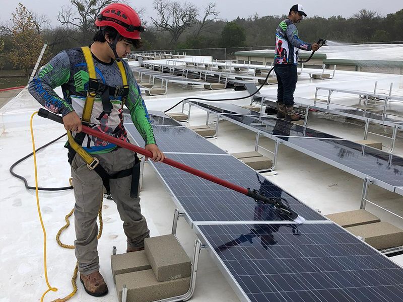 Two men are cleaning solar panels on a roof.