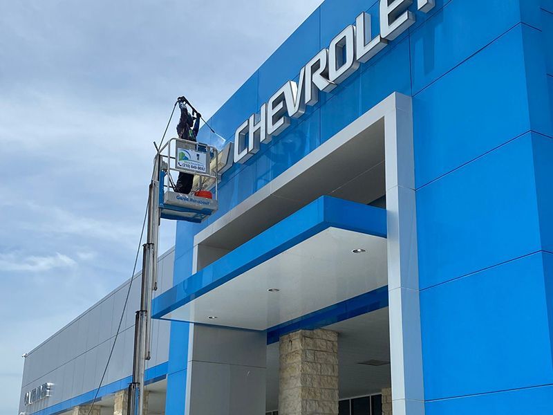 A man is cleaning the outside of a chevrolet car dealership.