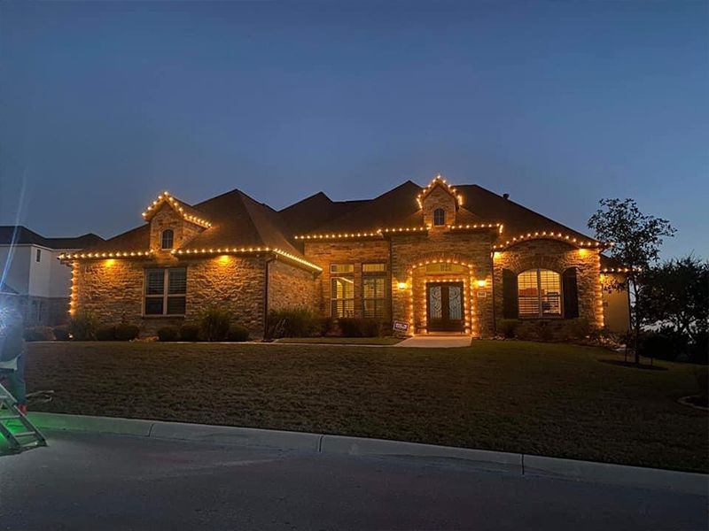 A large brick house is decorated with christmas lights at night.