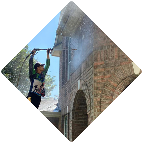 A man is cleaning a brick building with a high pressure washer.