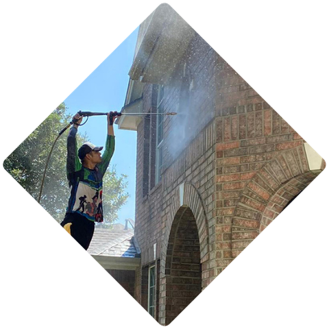 A man is cleaning a brick building with a high pressure washer.