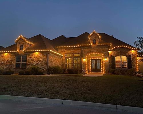 A large brick house is lit up with christmas lights at night.