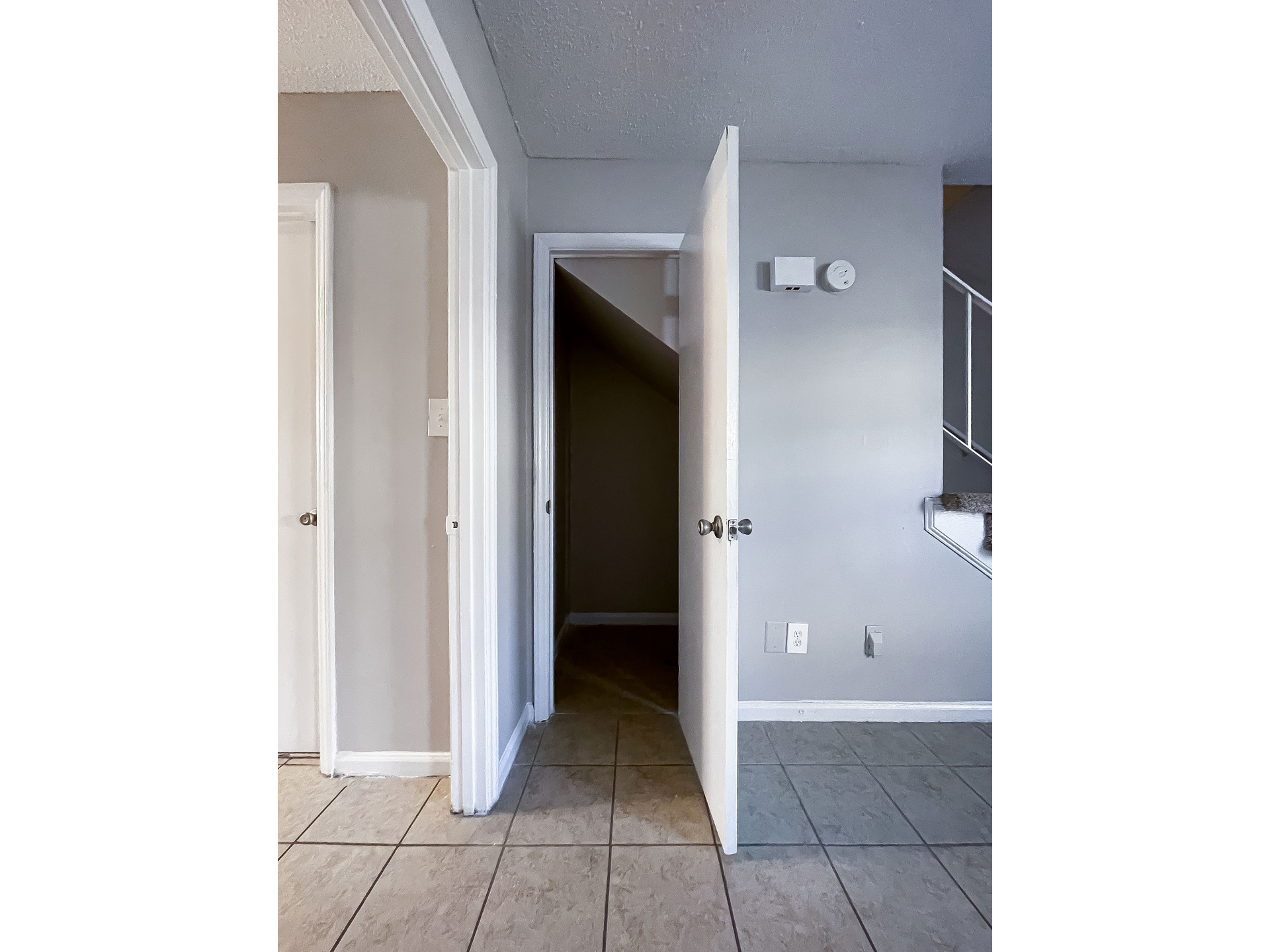 Interior hallway with open doors, gray walls, tile floor, and a stairway in the background