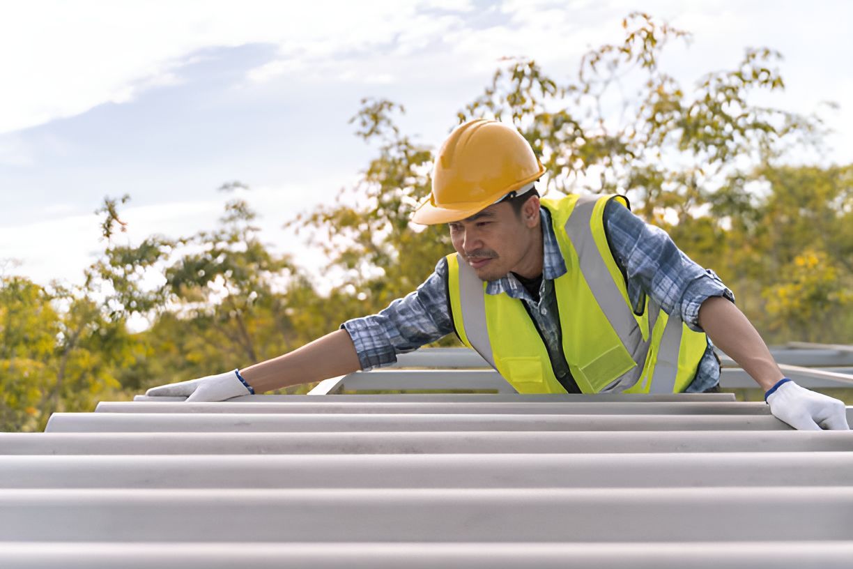 A construction worker in a safety helmet showcases a new shingle roofing installation on a roof.
