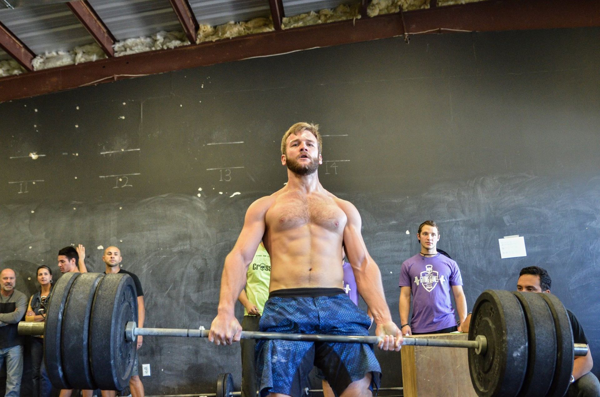 A shirtless man is lifting a barbell in a gym.