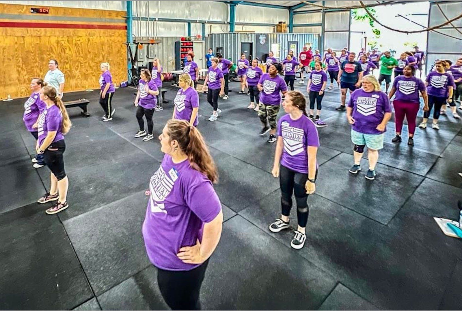 A group of people are standing in a gym wearing purple shirts.