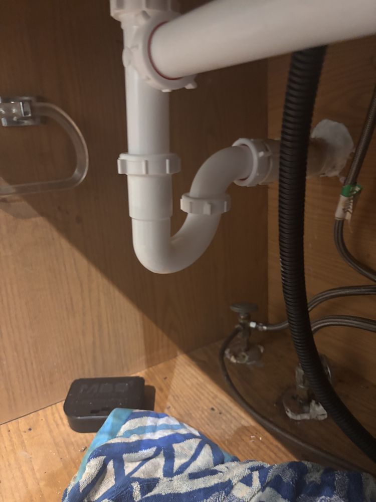 White plumbing under a bathroom sink, including a U-shaped trap and drainpipes.