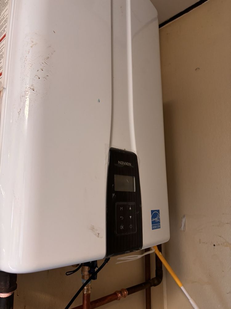 White tankless water heater mounted on a wall with digital display and copper pipes.