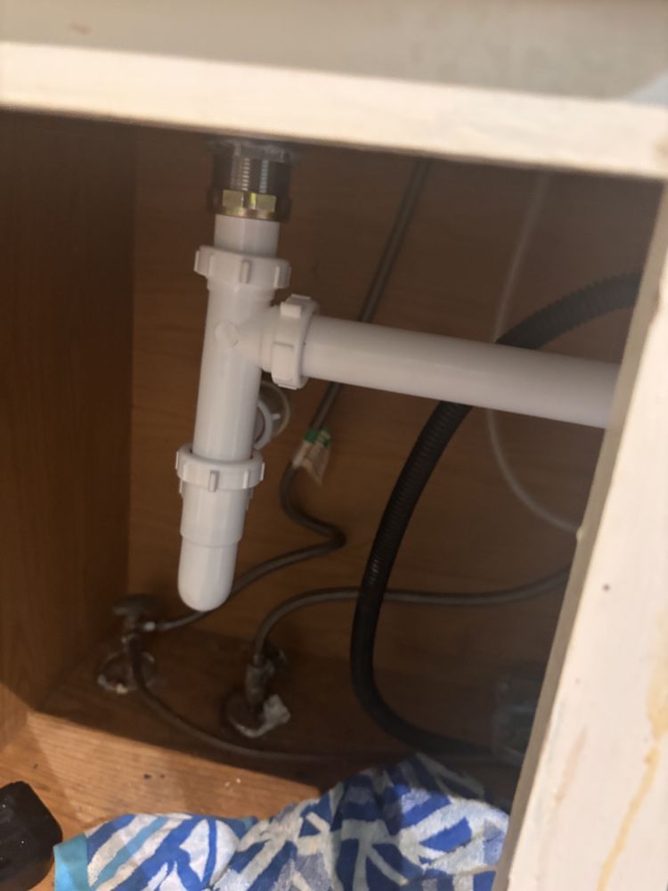 White sink drain pipes under a cabinet. Black water line visible.