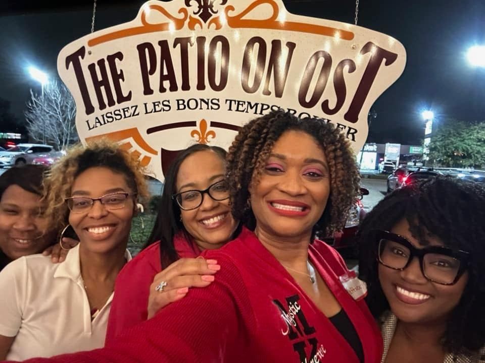 A group of women are posing for a picture in front of a sign that says the patio on ost