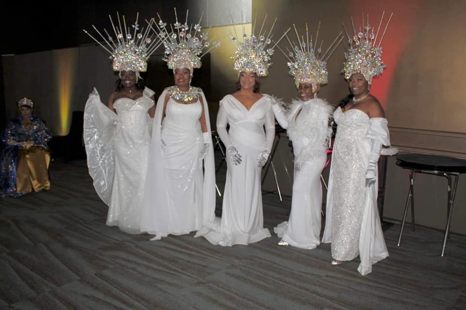 A group of women in white dresses and hats are standing next to each other.