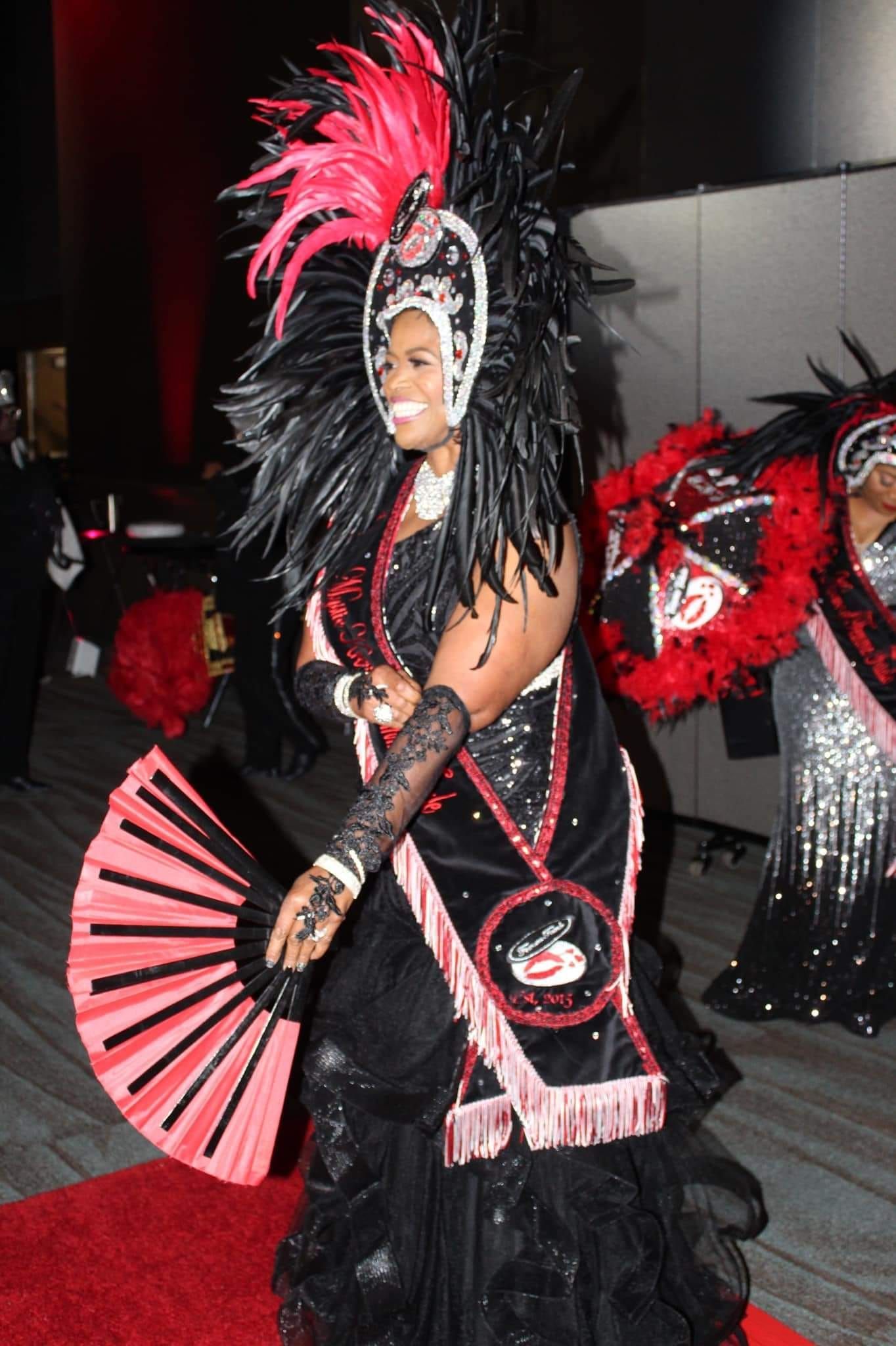 A woman in a black and red costume is holding a fan