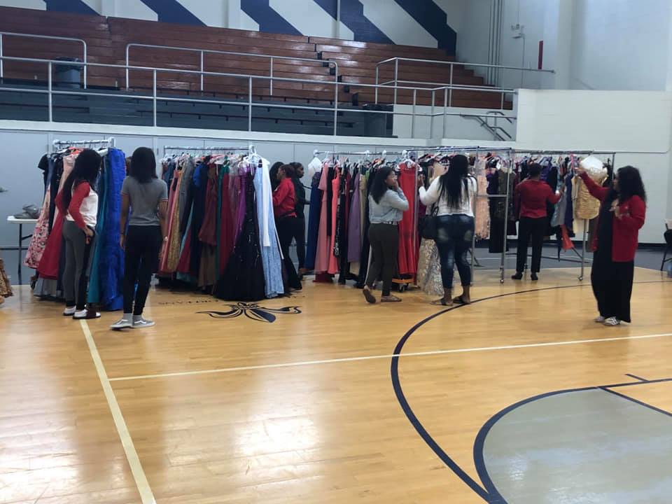A group of people are standing in a gym looking at clothes on racks