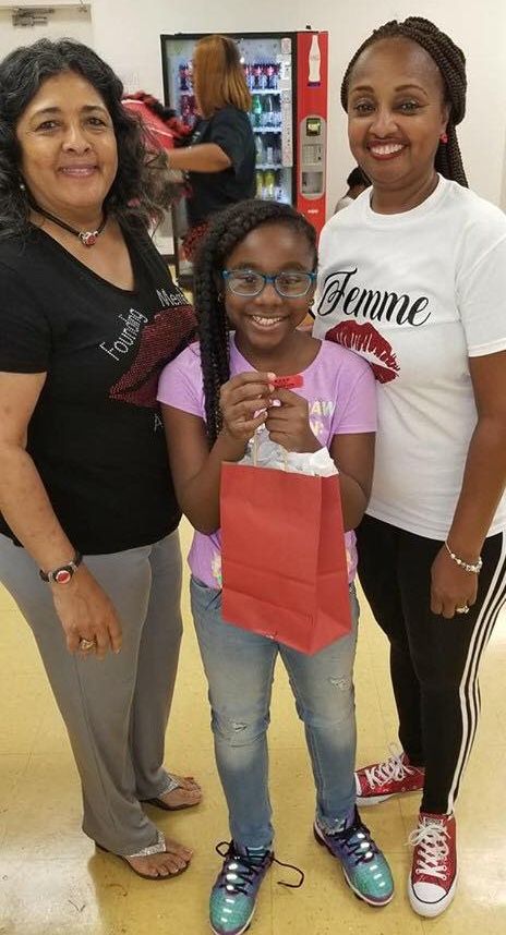 Three women are posing for a picture with a girl holding a red bag.
