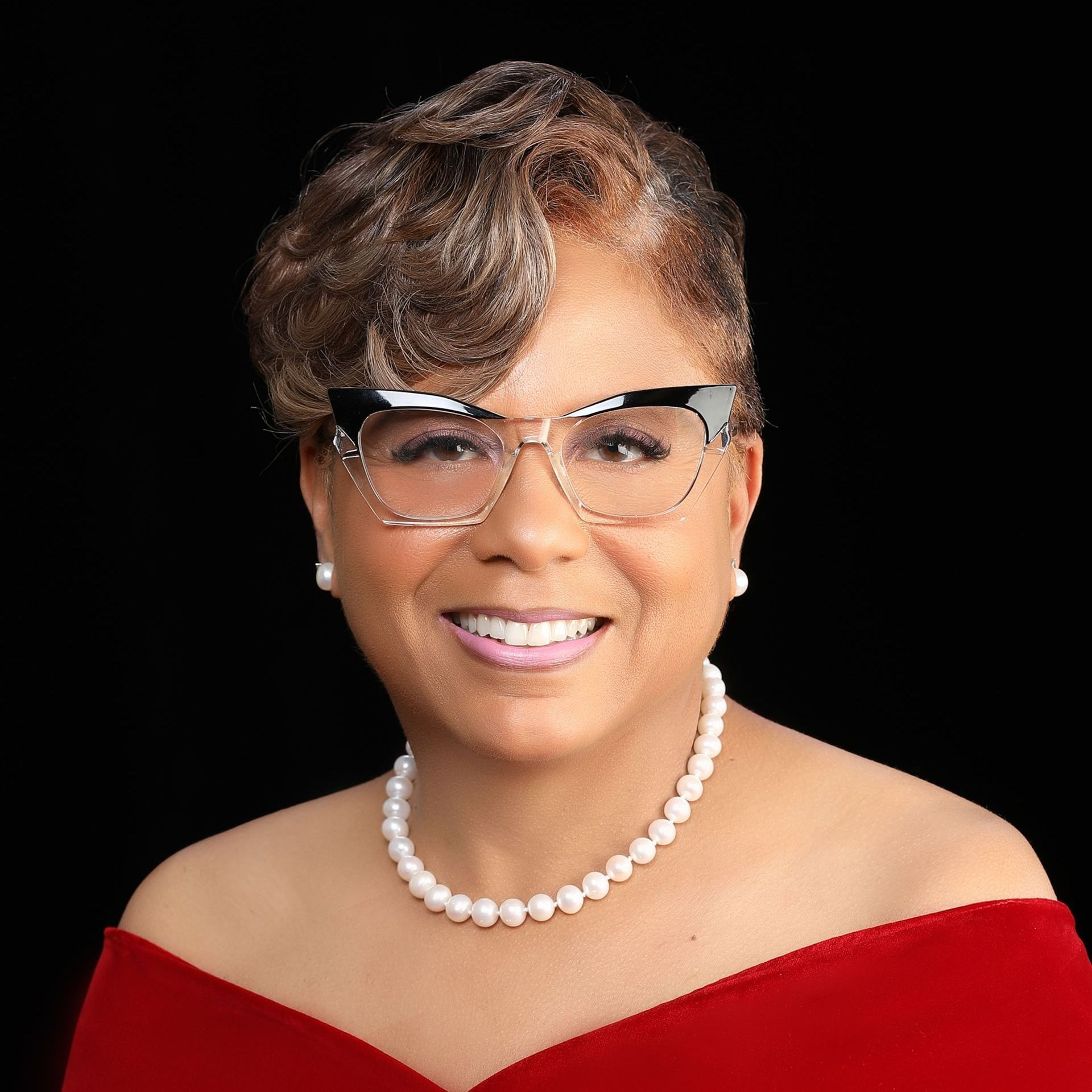 A woman wearing glasses and a pearl necklace is smiling for the camera.