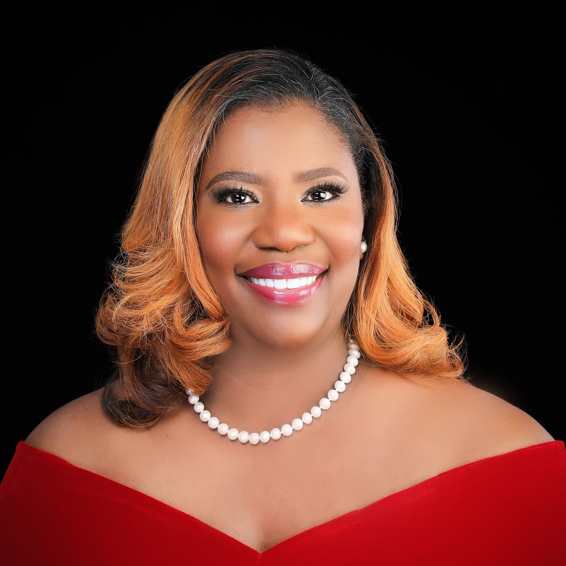 A woman wearing a red dress and a pearl necklace is smiling for the camera.
