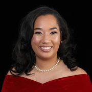 A woman wearing glasses and a pearl necklace is smiling for the camera.