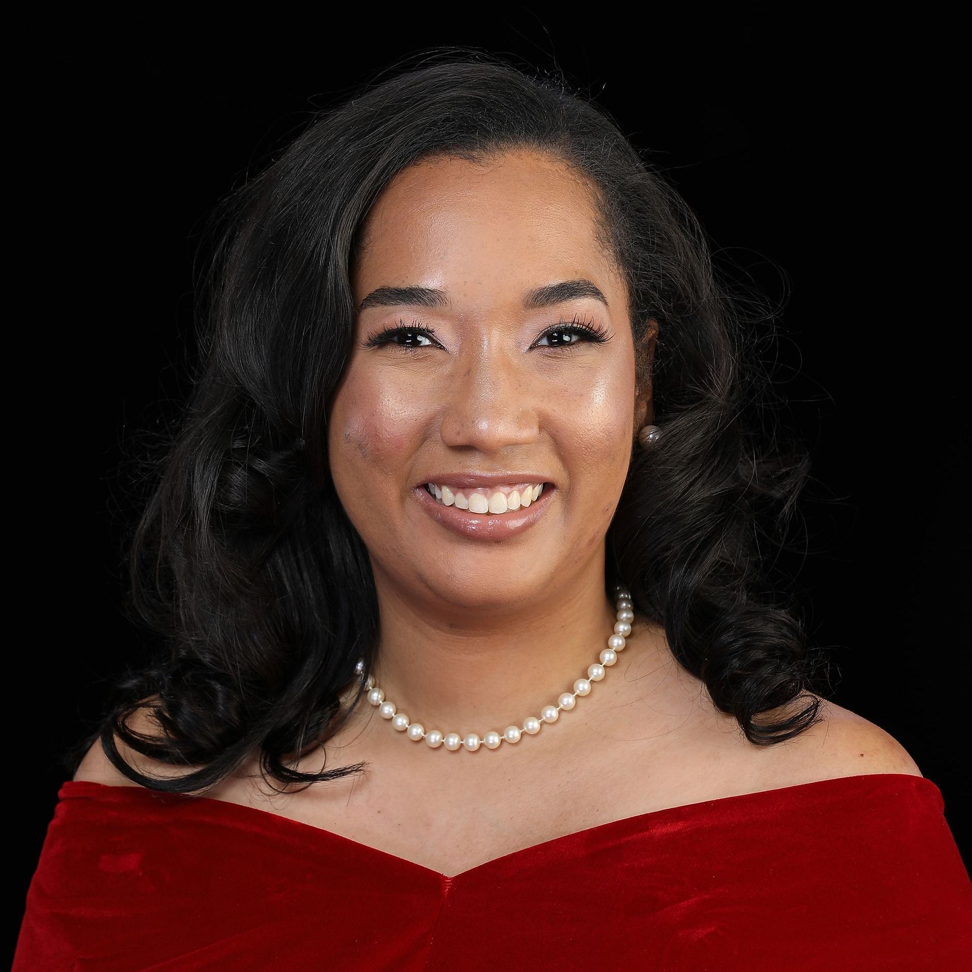A woman wearing a red dress and a pearl necklace is smiling for the camera.